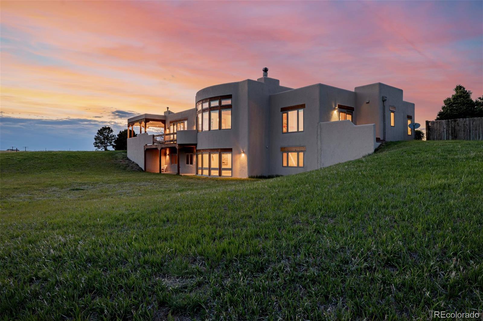 Adobe-style ranch house glowing at dusk under a pink sky on open grassland