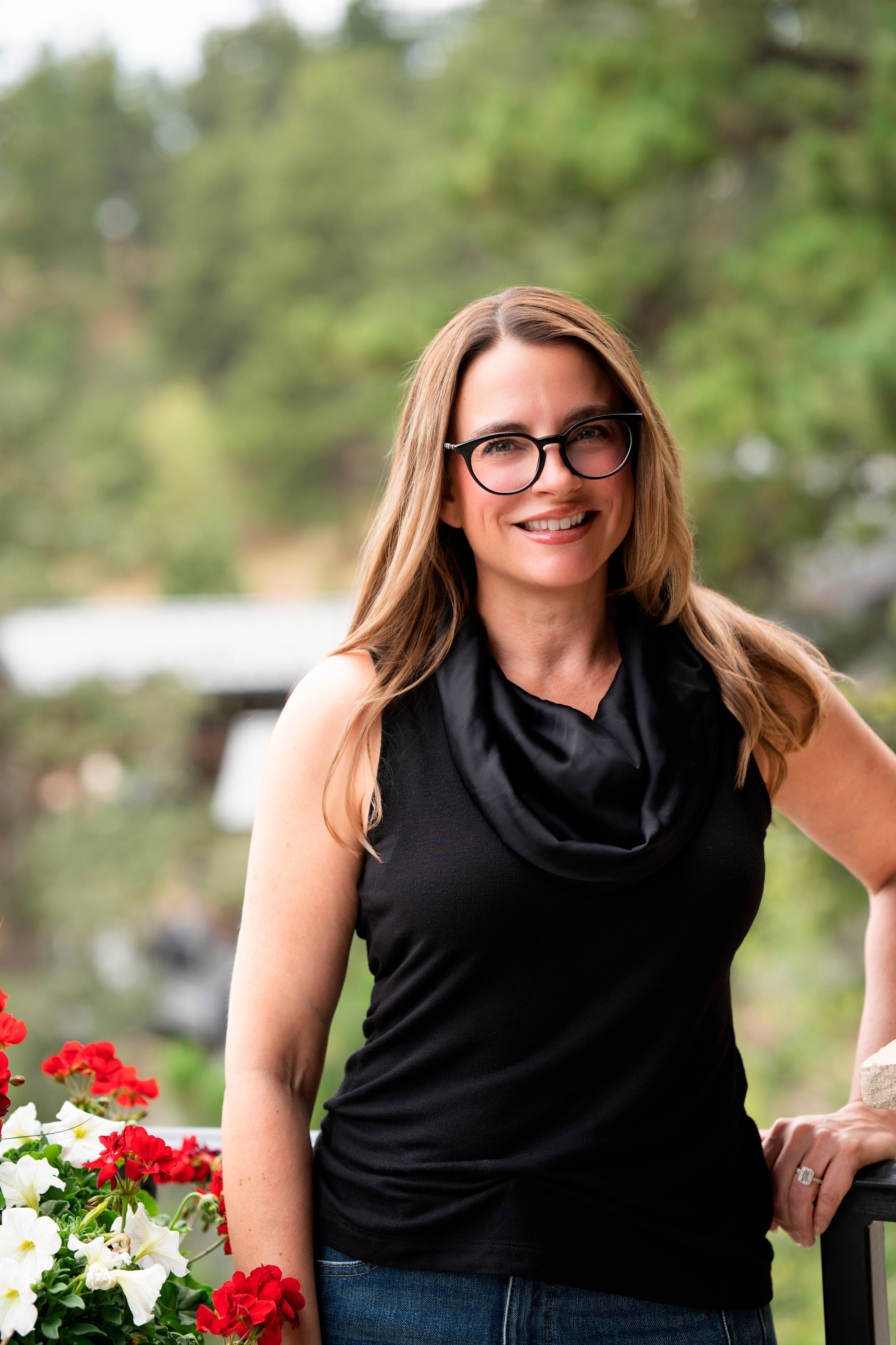 Portrait of Lisa Johnston Kane on a balcony with pine trees behind her